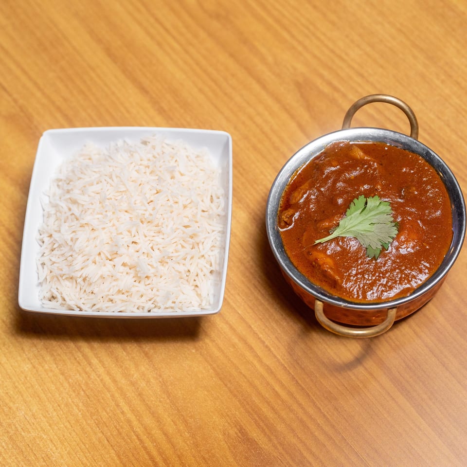 Basmati rice in a white dish served alongside red curry garnished with cilantro in a copper bowl.