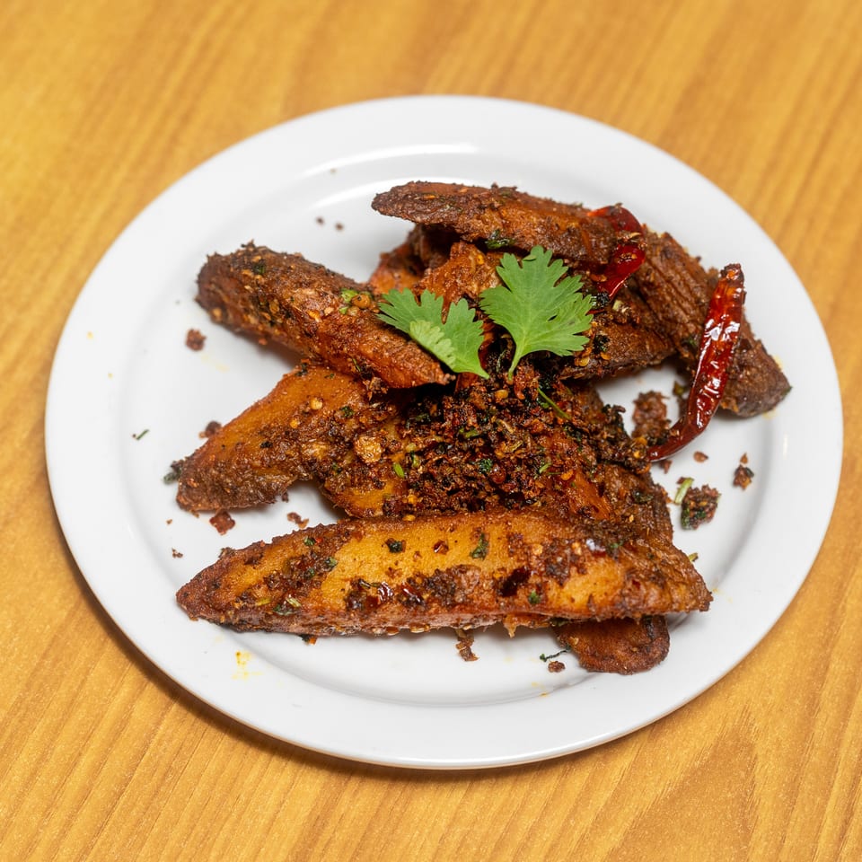 Spiced fried vegetable pieces garnished with cilantro and dried red chilies on a white plate.