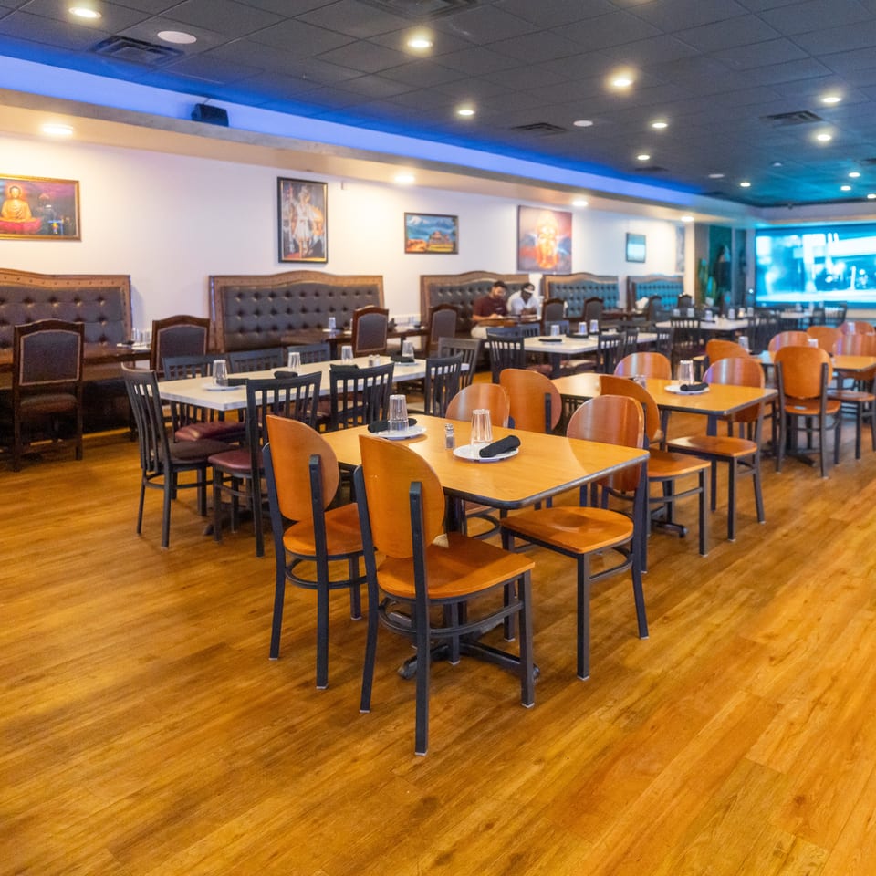 Spacious restaurant dining room with wooden tables, upholstered booths, framed artwork, blue accent lighting, and two diners.