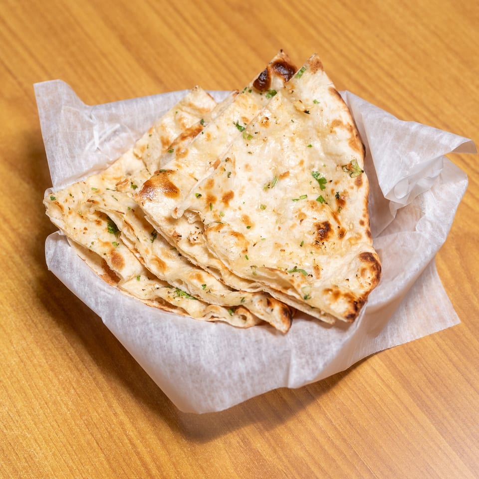 Stack of golden, herb-speckled flatbreads served in a paper-lined basket on a wooden table.