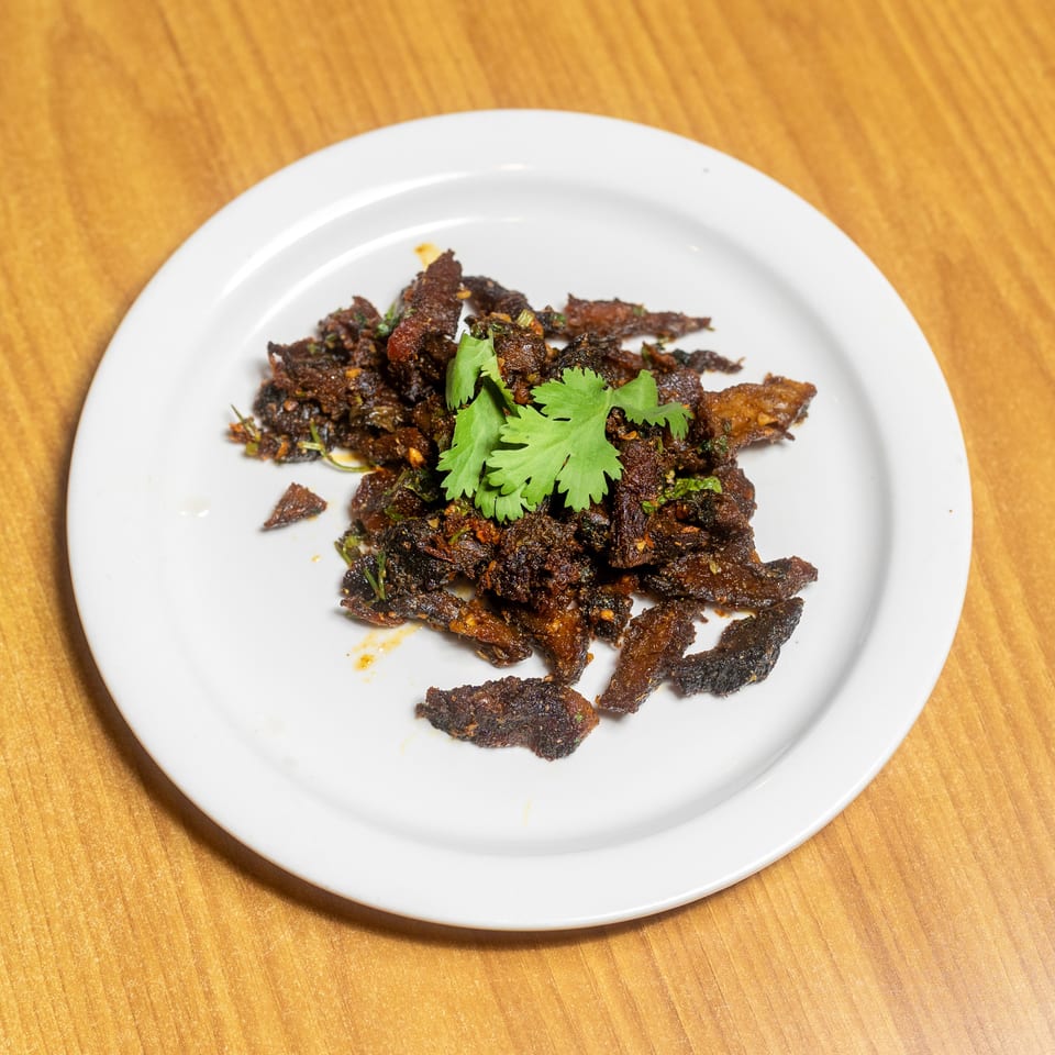 Plate of crispy spiced meat pieces garnished with fresh cilantro on a wooden table.