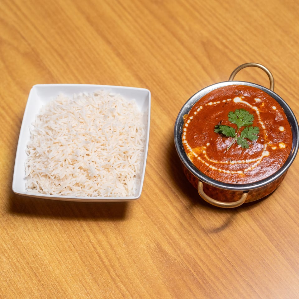 Basmati rice served beside creamy red curry garnished with cilantro in a handled metal bowl.