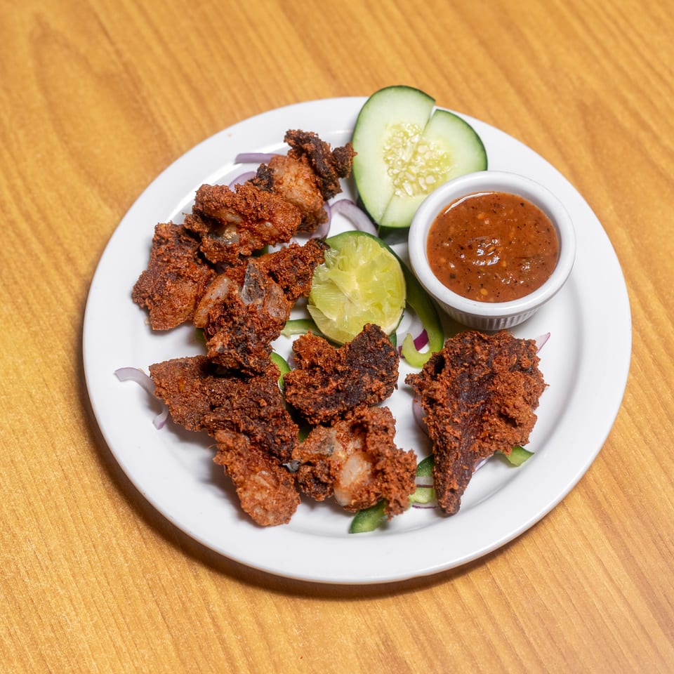 Plate of crispy fried chicken pieces with dipping sauce, cucumber, lime, and sliced onions on a wooden table.