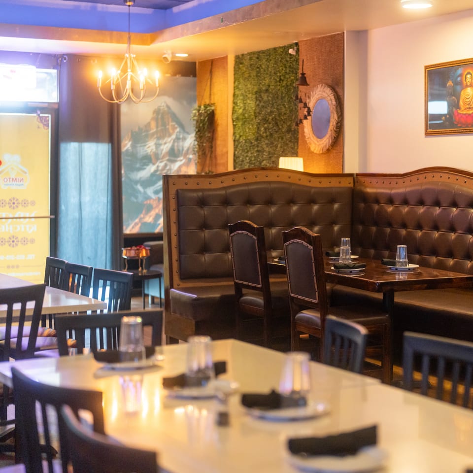 Warmly lit restaurant interior with dark leather booths, set tables, chandelier, greenery wall, and Buddhist artwork.