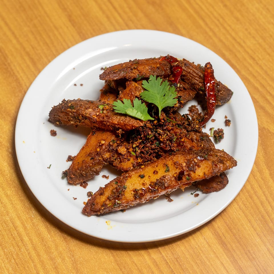 Crispy spiced fried vegetable pieces garnished with cilantro and dried red chilies on a white plate.