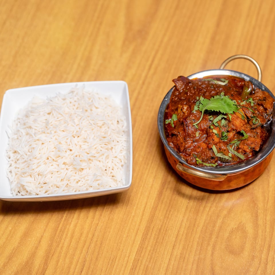 Basmati rice served beside a bowl of rich red curry garnished with fresh cilantro on a wooden table.